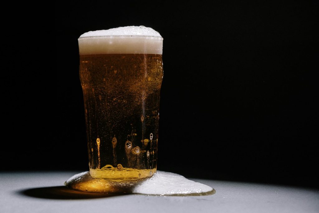 A studio shot of a frothy and overflowing pint of golden beer against a dark backdrop.